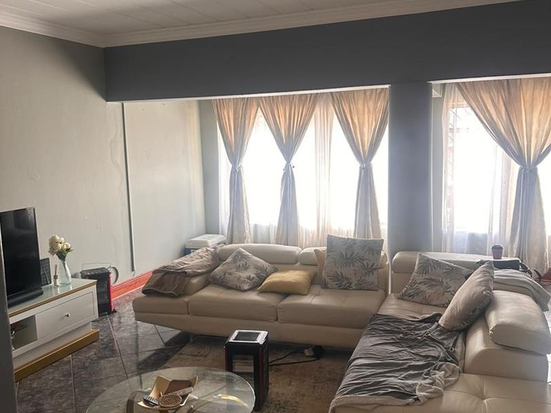 A living room featuring tiled flooring, large windows allowing natural light, and a coved ceiling. The space requires minor cosmetic repairs to walls.