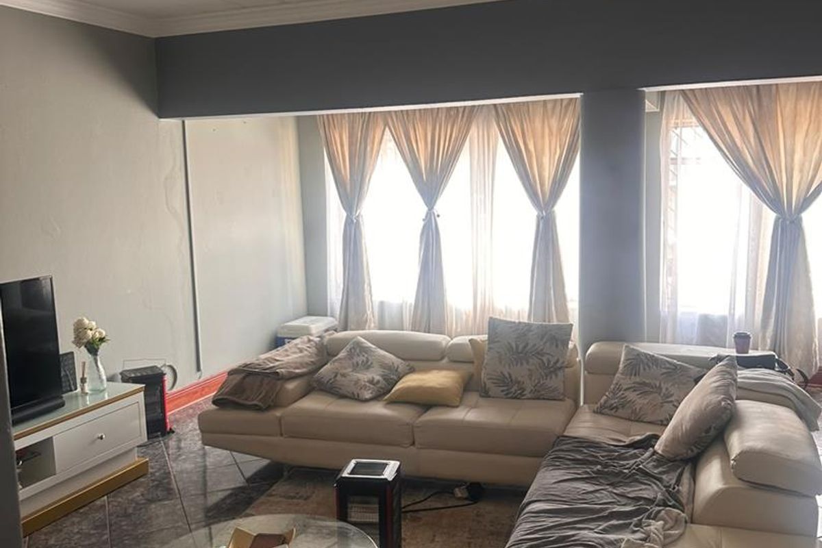 A living room featuring tiled flooring, large windows allowing natural light, and a coved ceiling. The space requires minor cosmetic repairs to walls.