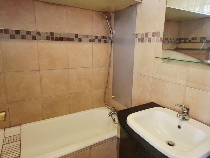 A functional bathroom featuring a bathtub with a handheld shower, a vanity basin with a granite countertop, and tiled wall finishes.
