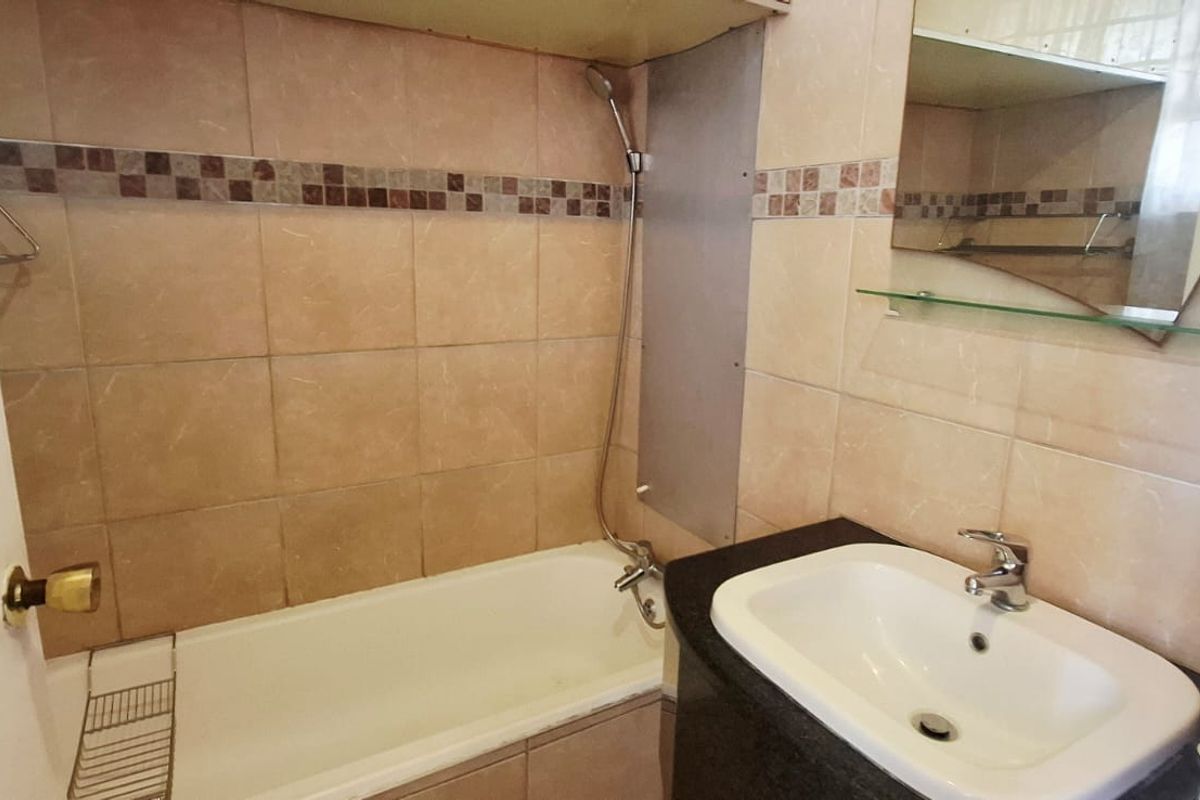 A functional bathroom featuring a bathtub with a handheld shower, a vanity basin with a granite countertop, and tiled wall finishes.
