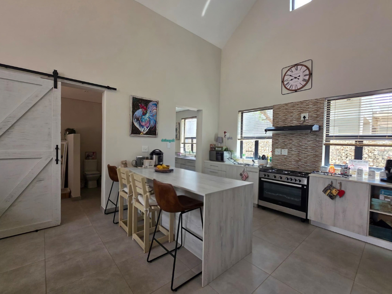 Modern kitchen featuring a central island, gas stove with extractor, tiled backsplash, and high vaulted ceilings, complemented by a sliding barn door.