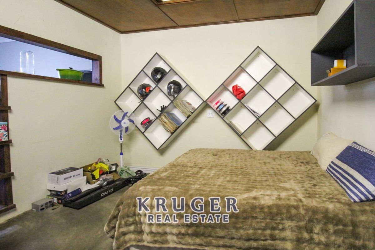 A bedroom featuring built-in diamond-shaped wall shelving and a high-level interior window, providing a unique layout with potential for modernization.