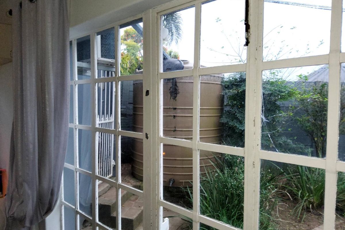 View from inside looking out at a rear garden area featuring a large water storage tank, brick steps, and white-framed french doors.