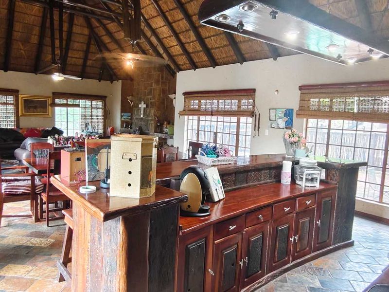 Spacious open-plan living and kitchen area featuring a high thatched ceiling with exposed rafters, stone fireplace, and durable slate tile flooring throughout.
