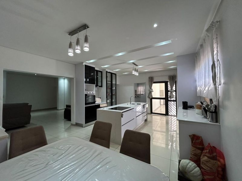 Modern open-plan kitchen and dining area featuring a central island with integrated hob, sleek cabinetry, and polished tiled flooring.
