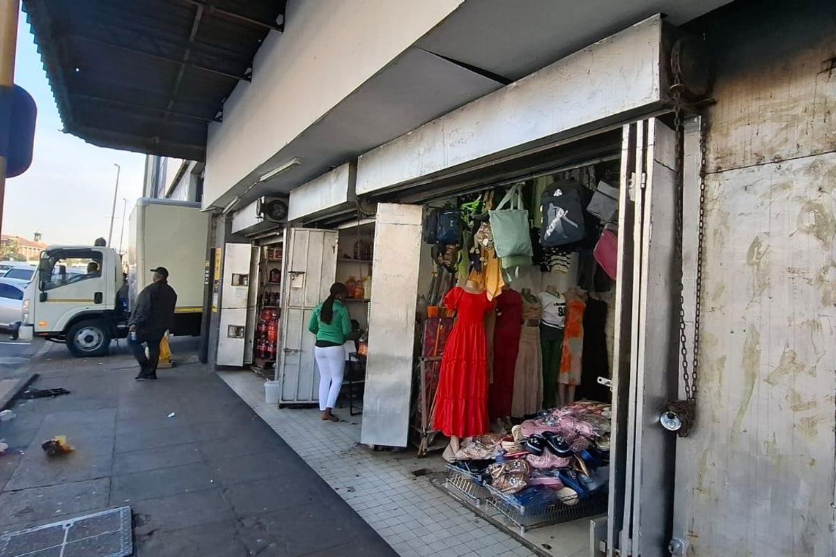 Street-level view of a commercial shop front featuring metal security shutters, a protective awning, and direct access from the public pavement.