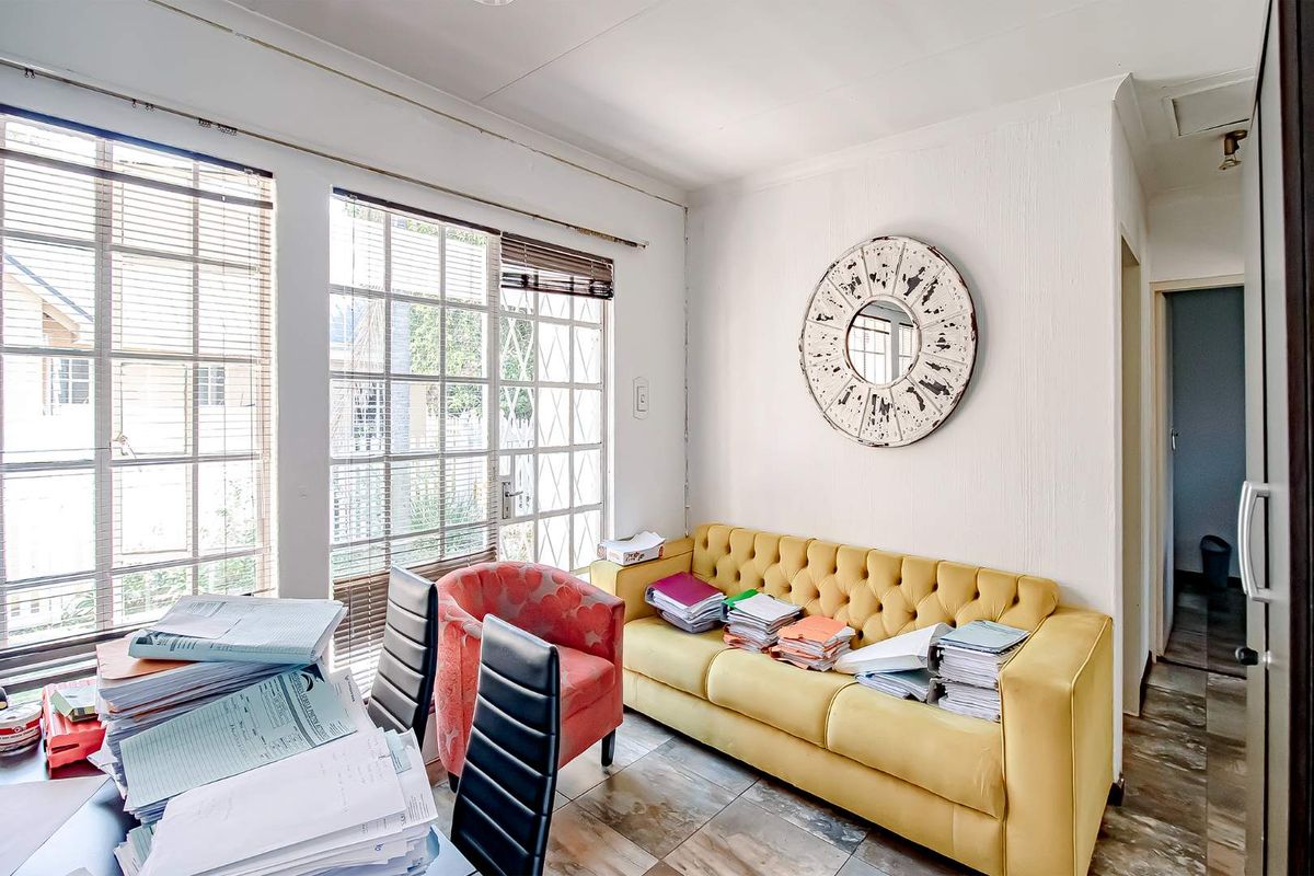 A multi-purpose living area featuring large windows with security bars, tiled flooring, and direct access to the exterior.