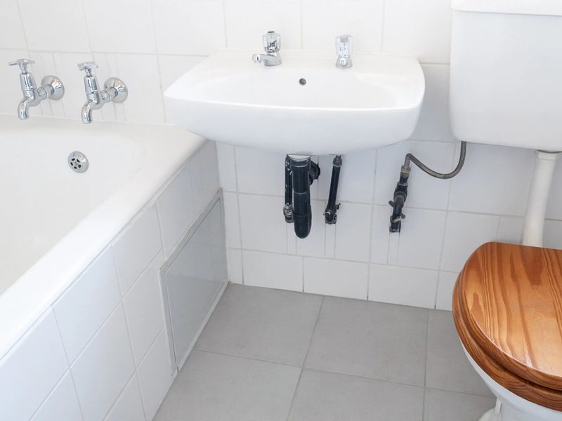 A functional bathroom featuring a white bathtub, wall-mounted basin, and toilet with neutral wall and floor tiling.