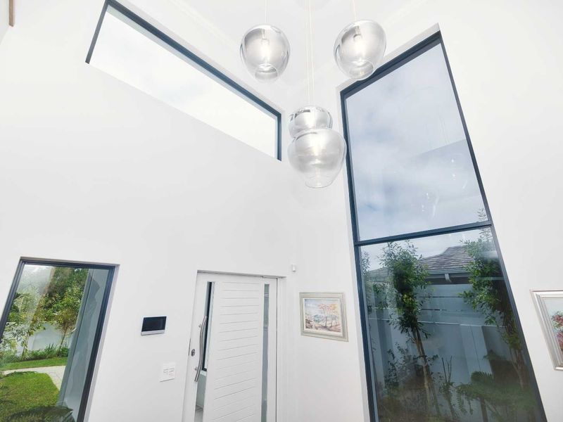 A bright, double-volume entrance hall featuring expansive floor-to-ceiling windows, clerestory windows, and a modern front door, creating a light-filled and welcoming space.
