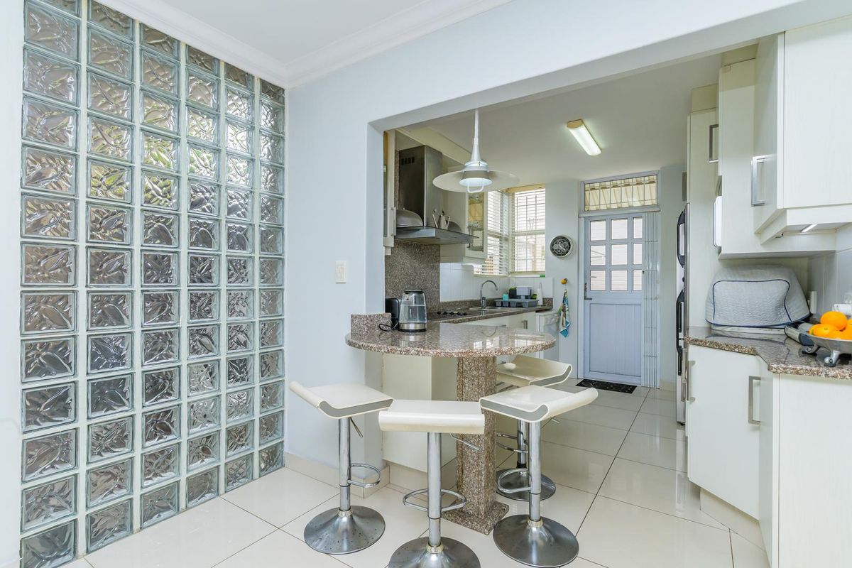 A functional kitchen featuring a granite breakfast bar, glass block feature wall, tiled flooring, and direct access to an exterior door.