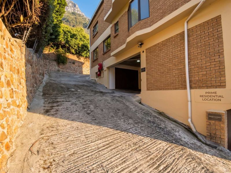 Exterior view of the apartment building entrance featuring a brick facade, concrete driveway, and stone retaining wall.