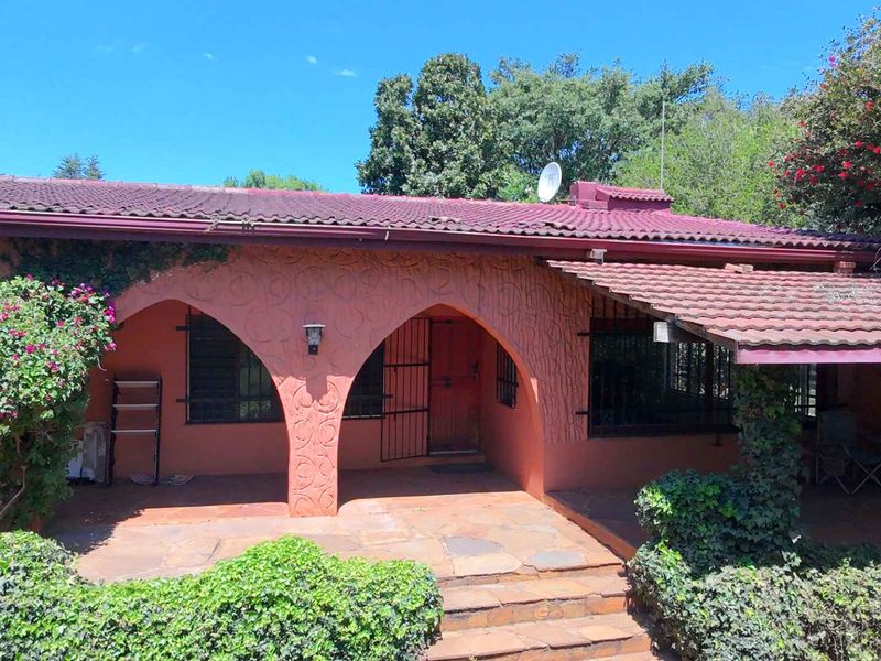 A rear exterior view of a house featuring a covered patio with arched architectural details, terracotta roofing, and stone paving.