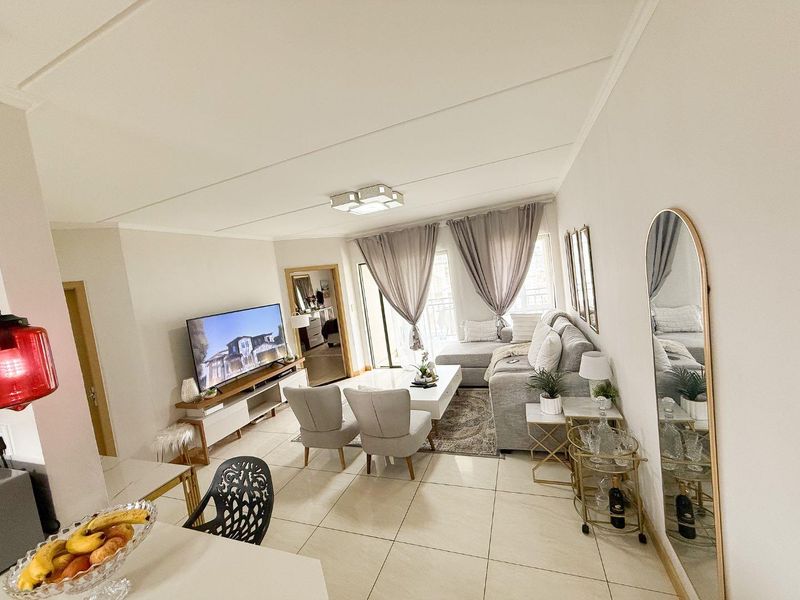 A bright and well-maintained living room featuring large format floor tiles, neutral walls, and a sliding glass door leading to an outdoor area.