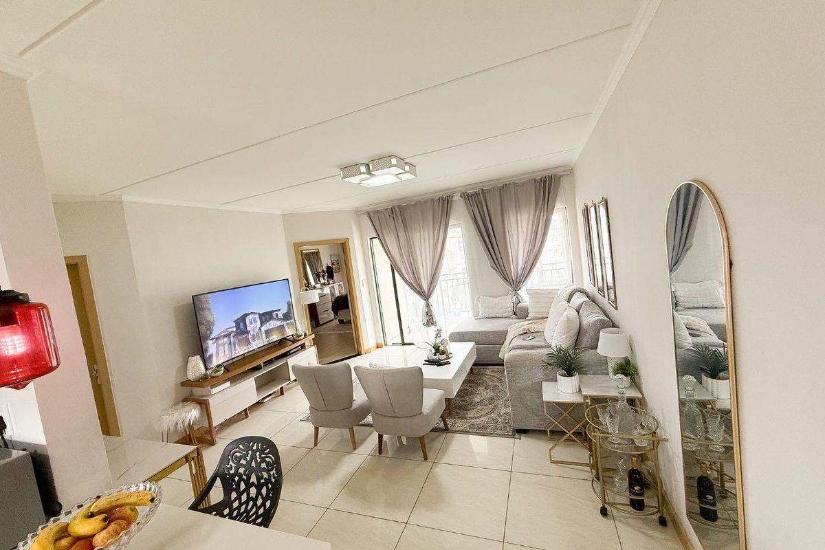 A bright and well-maintained living room featuring large format floor tiles, neutral walls, and a sliding glass door leading to an outdoor area.