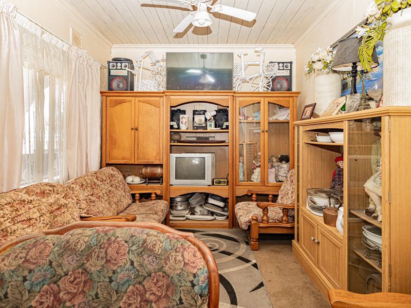 A living room featuring a ceiling fan and timber-look ceiling paneling, currently presenting with dated finishes and worn flooring.
