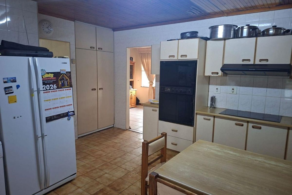 A dated kitchen featuring built-in cabinetry, integrated oven, and hob, with tiled flooring and a timber-paneled ceiling.
