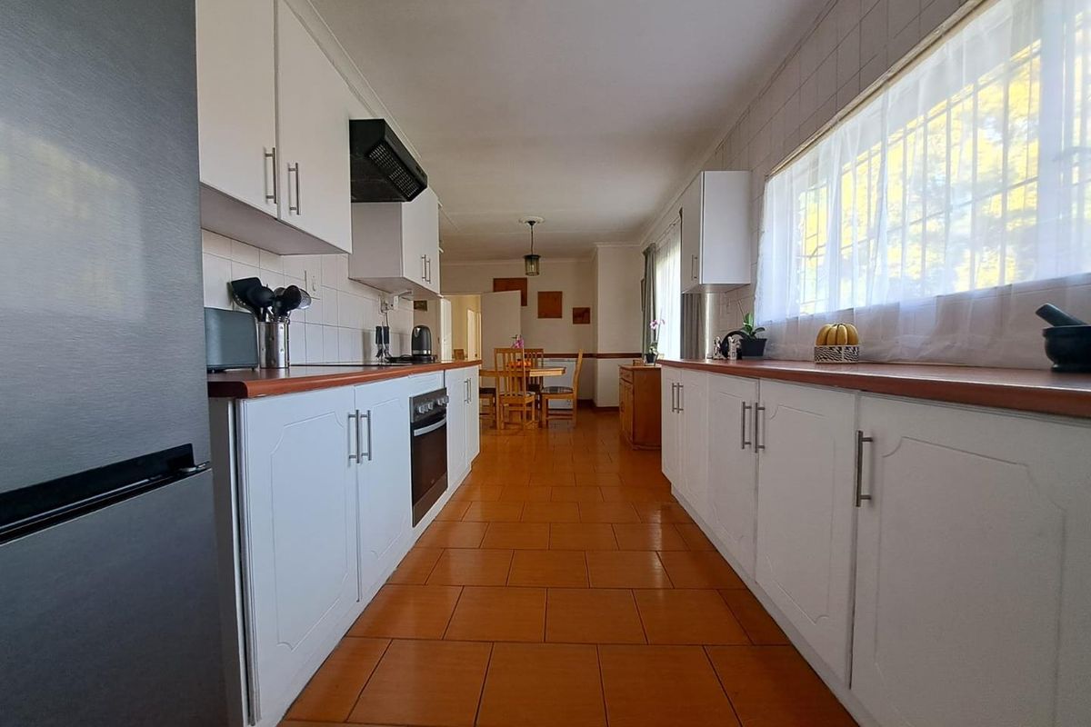Galley-style kitchen featuring white cabinetry, wood-tone countertops, tiled flooring, and integrated oven with extractor fan, leading into an adjacent dining area.