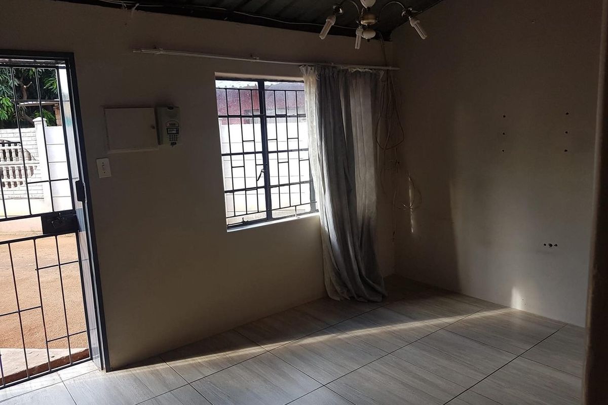 An empty living room featuring tiled flooring, security gates, and burglar bars, with exposed ceiling and wall wiring requiring attention.