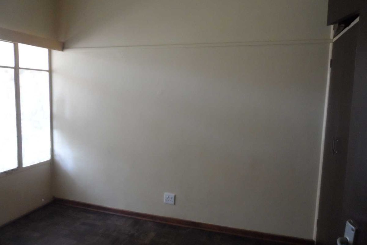 An empty bedroom featuring original parquet flooring, a built-in cupboard, and a large window allowing natural light.