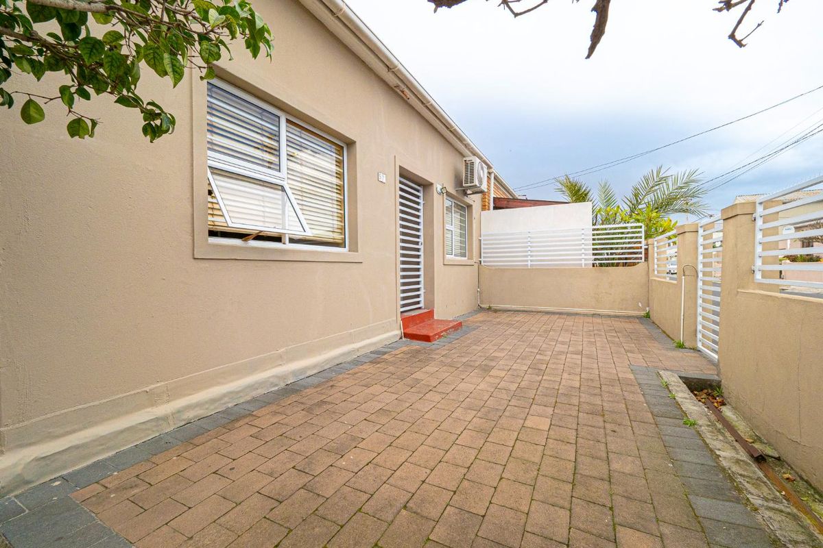 A paved rear courtyard area featuring a security gate, boundary wall with slatted fencing, and an external air conditioning unit.