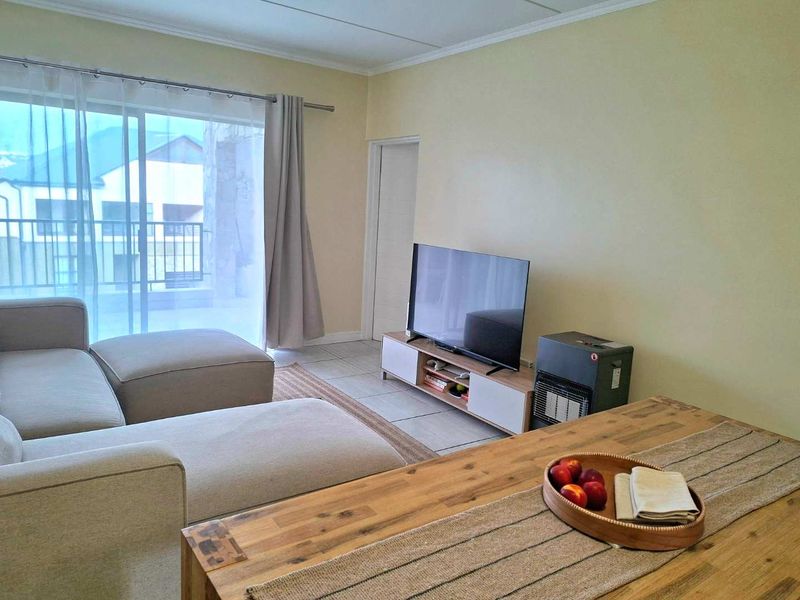 A comfortable living room featuring tiled flooring, neutral walls, and a large sliding glass door providing access to an outdoor balcony area.