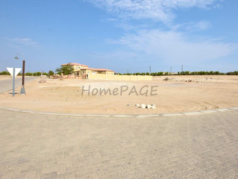 A vacant residential plot featuring paved road access, street lighting, and a boundary wall, ready for development.