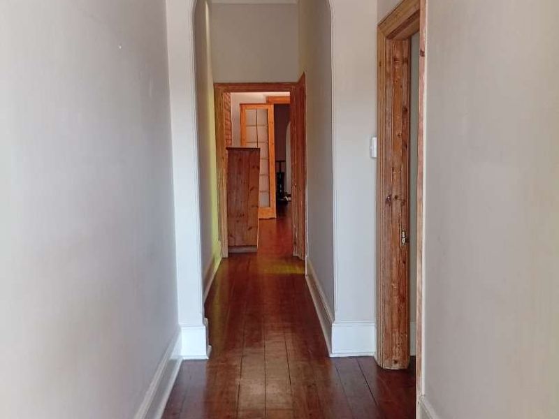 A bright, empty hallway featuring polished timber flooring, classic archway detailing, and neutral wall finishes connecting multiple rooms.