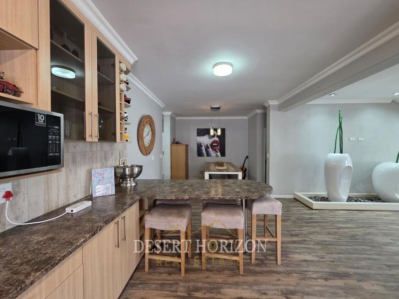 Open-plan living and kitchen area featuring wood-look laminate flooring, modern cabinetry, and integrated lighting, creating a cohesive and functional multi-purpose space.