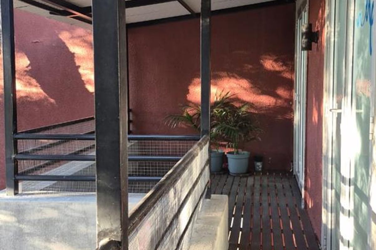 A covered outdoor balcony featuring timber decking, metal railings, and steel support columns, providing access to the building interior.