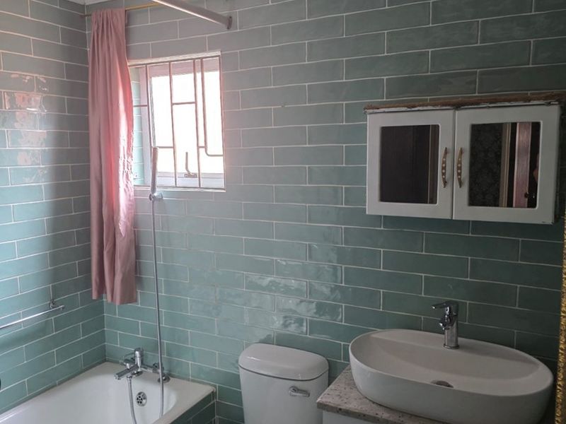 A functional bathroom featuring green subway wall tiles, a built-in bathtub, a vessel sink vanity, and a wall-mounted medicine cabinet.