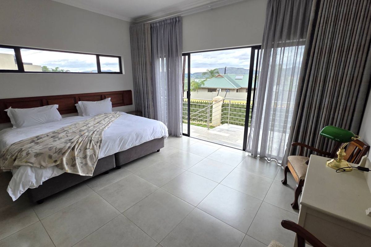 Spacious bedroom featuring large sliding glass doors leading to a private balcony, neutral floor tiles, and a built-in wooden headboard.