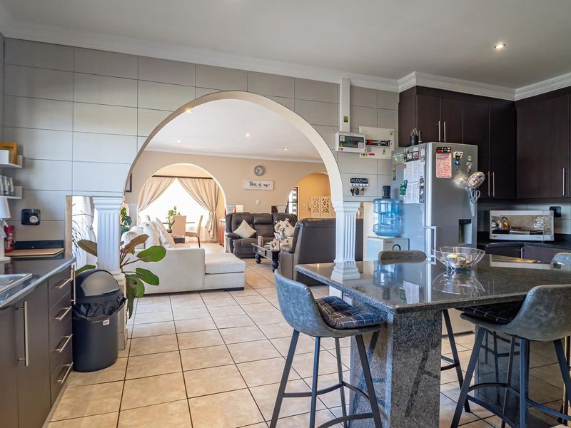 Open-plan kitchen and living area featuring dark wood cabinetry, granite countertops, a central island, and tiled flooring with arched architectural transitions.