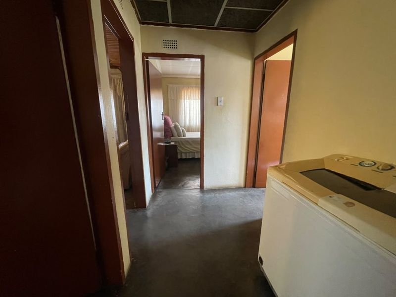 A functional hallway connecting multiple rooms, featuring concrete flooring, wooden door frames, and a tiled ceiling, requiring cosmetic updates.