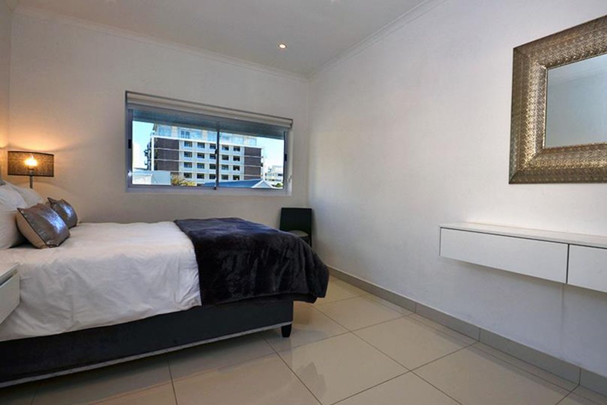 A well-maintained bedroom featuring tiled flooring, recessed downlighting, and a wall-mounted floating vanity unit.