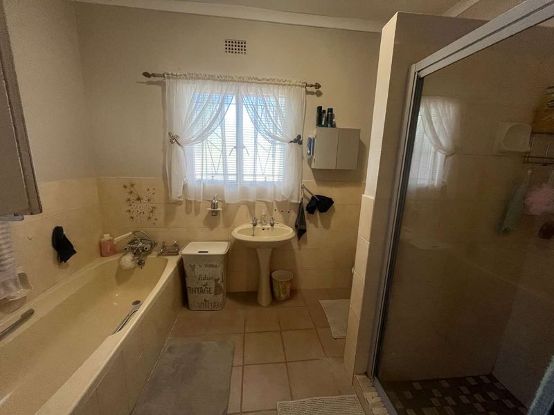 A functional bathroom featuring a pedestal basin, built-in bathtub, and a separate shower enclosure with neutral wall and floor tiling.