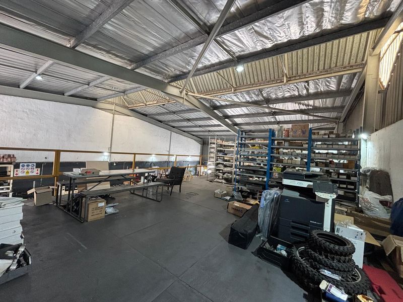Spacious industrial mezzanine area featuring exposed steel roof trusses, metal roofing, and safety railings, suitable for storage or workshop use.