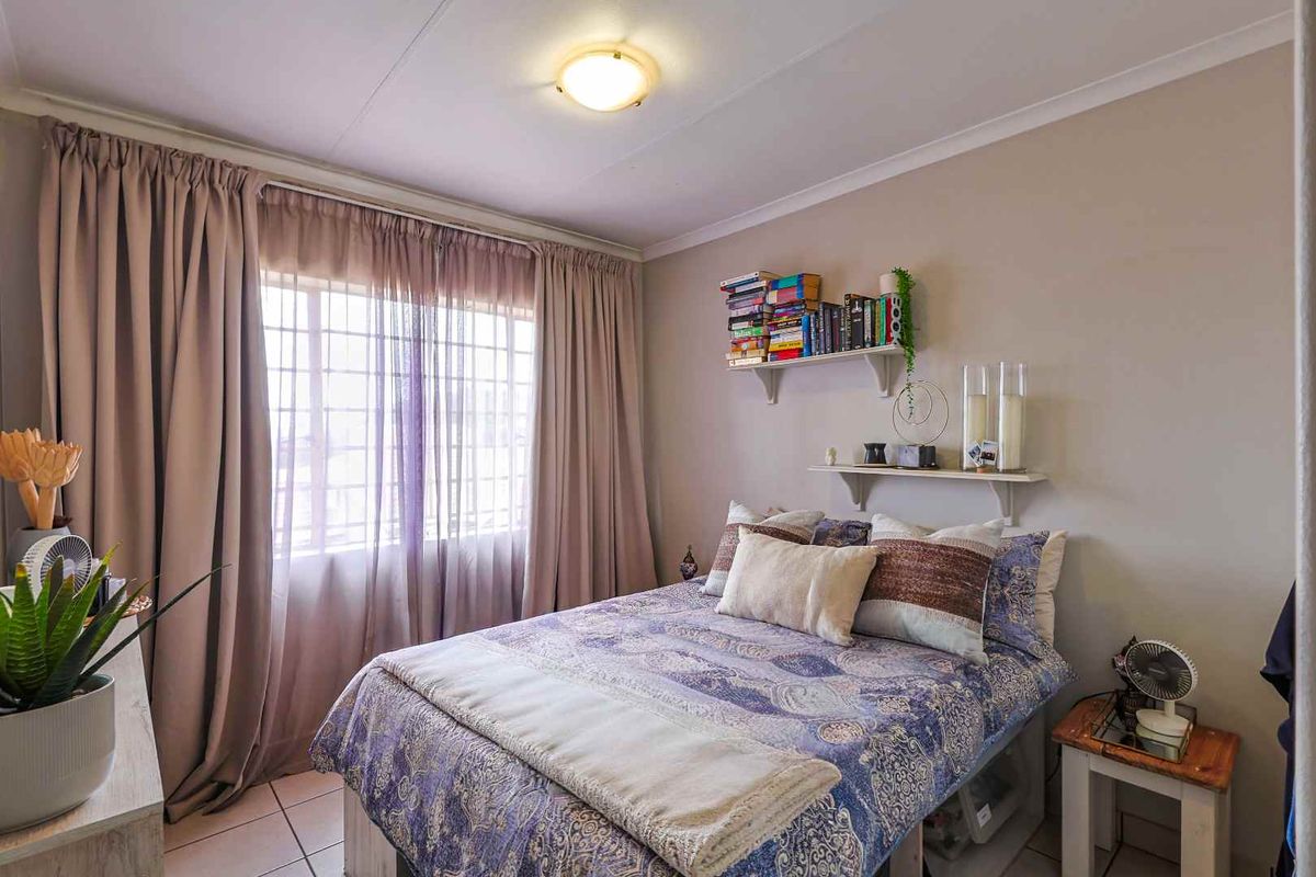 A cozy bedroom featuring tiled flooring, neutral wall tones, and a window dressed with full-length curtains.