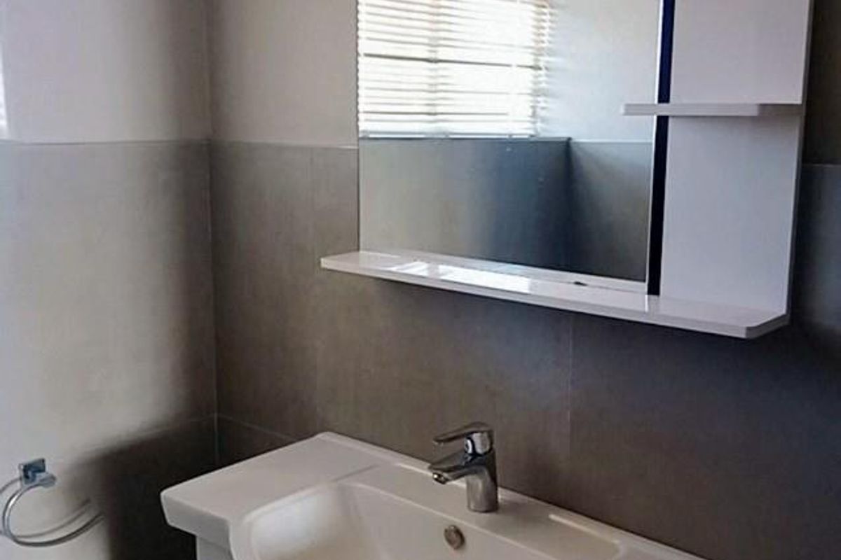 A clean, modern bathroom featuring a white vanity cabinet with a ceramic basin, mixer tap, and a matching wall-mounted mirror with integrated shelving.
