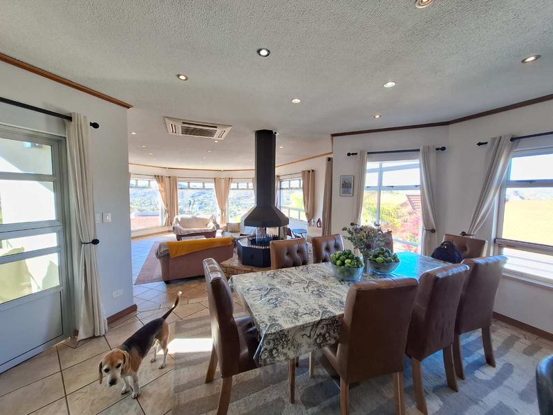 Spacious open-plan living and dining area featuring a central freestanding fireplace, tiled flooring, and large windows with scenic views.
