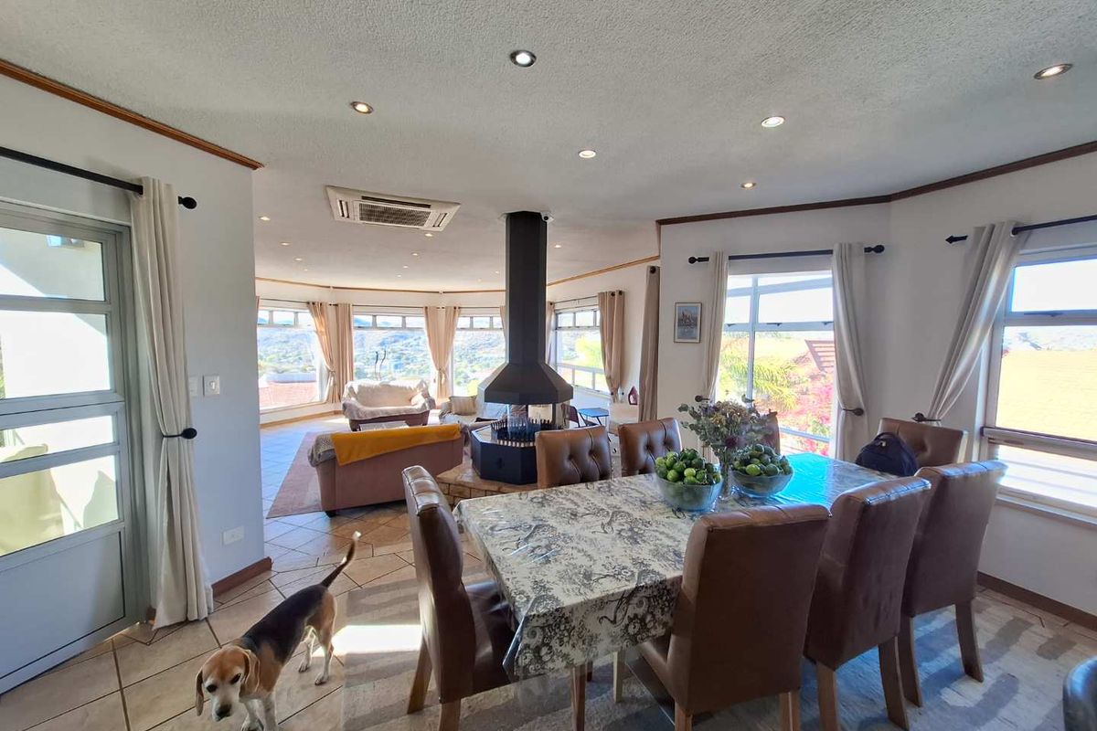 Spacious open-plan living and dining area featuring a central freestanding fireplace, tiled flooring, and large windows with scenic views.