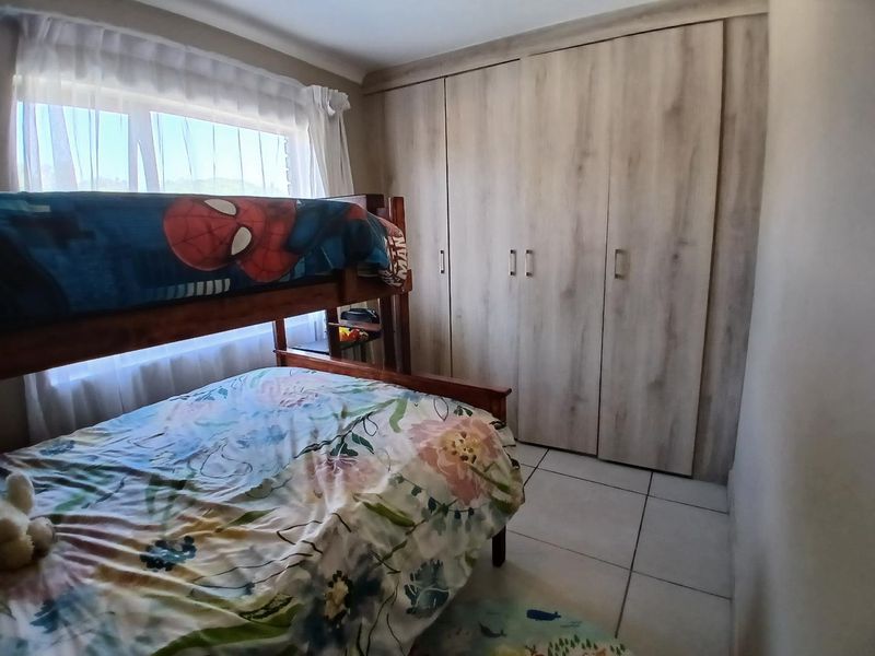 A functional bedroom featuring light wood-finish built-in cupboards and neutral tiled flooring, providing ample storage and a clean, practical layout.
