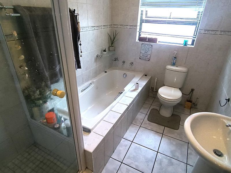A functional bathroom featuring a built-in bathtub, separate shower enclosure, pedestal basin, and toilet with neutral ceramic tiling throughout.