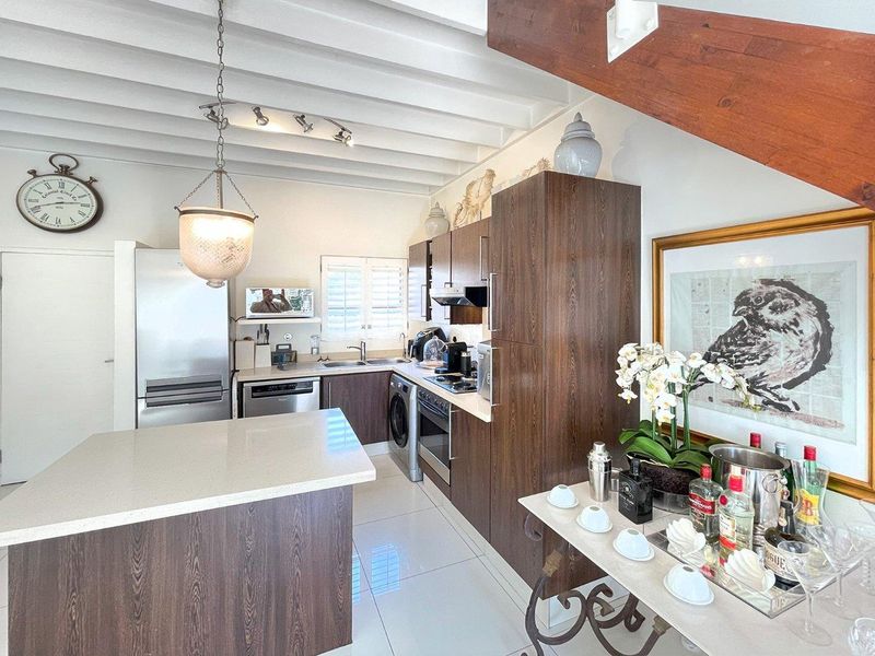 Modern kitchen featuring dark wood cabinetry, a central island, stainless steel appliances, and exposed white ceiling beams, creating a bright and functional cooking space.
