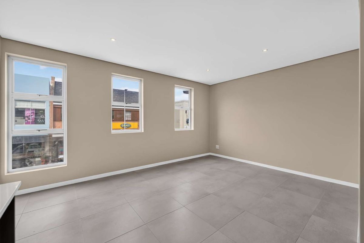 A bright, empty living area featuring neutral walls, modern tiled flooring, and recessed downlights, offering a clean and versatile space.