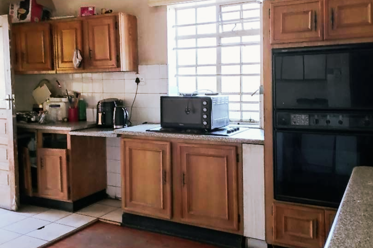 A dated kitchen featuring wooden cabinetry, a built-in double oven, and a mix of tiled and laminate flooring, requiring cosmetic updates.