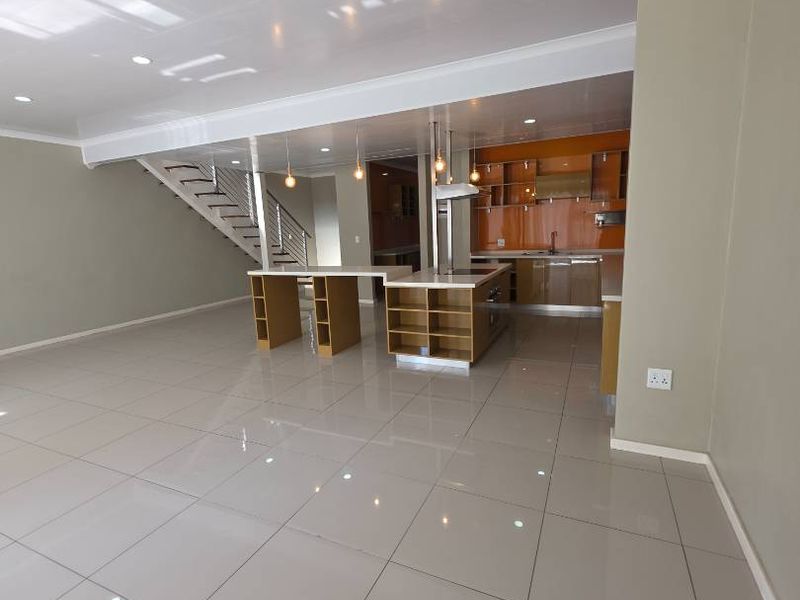 Spacious open-plan living and kitchen area featuring modern cabinetry, a central island, tiled flooring, and an integrated staircase.