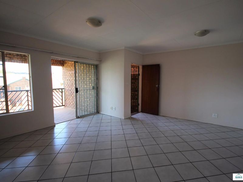 An empty, tiled living room featuring a sliding glass door with a security gate leading to an outdoor balcony area.