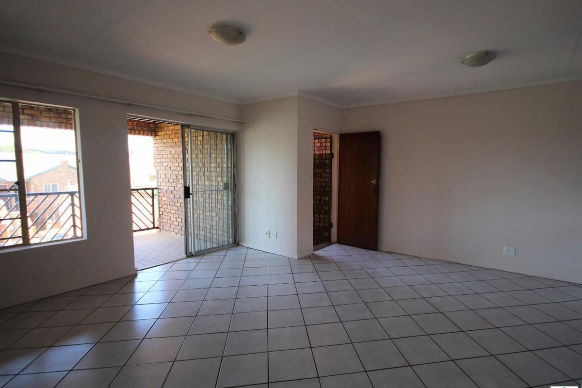 An empty, tiled living room featuring a sliding glass door with a security gate leading to an outdoor balcony area.
