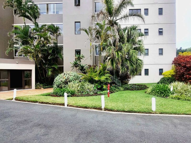 The front exterior of the Malindi apartment complex featuring a well-maintained landscaped garden, paved driveway, and modern building facade.