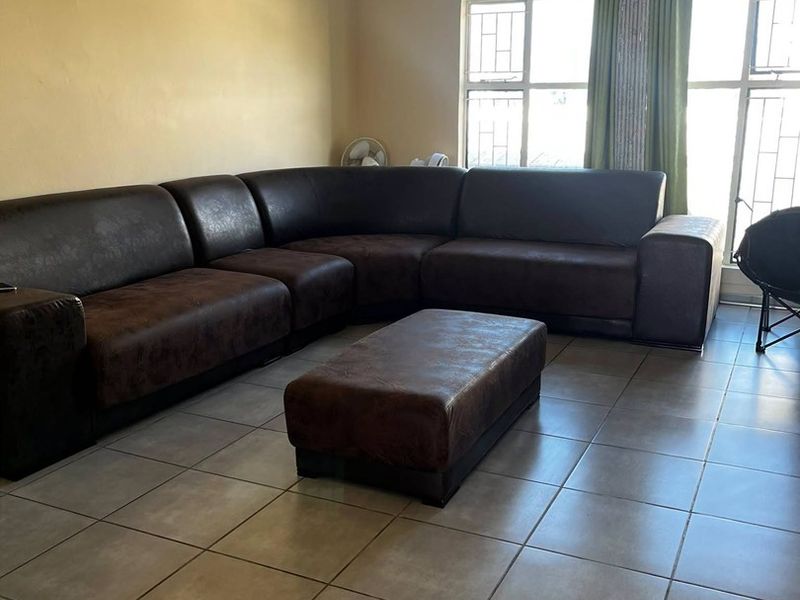 A living room featuring neutral tiled flooring, large windows with security bars, and simple cornicing, providing a functional and well-lit space.